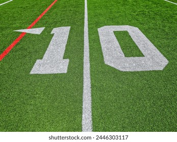 Football Field Turf. Bright green turf football field with white sidelines and yard line markings. Focus on the ten yard line marker. Overhead view. - Powered by Shutterstock