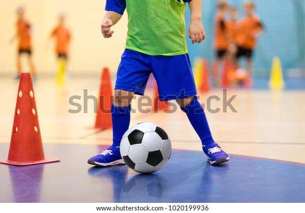 Football futsal\
training for children. Soccer training dribbling cone drill. Indoor\
soccer young player with a soccer ball in a sports hall. Player in\
blue uniform. Sport\
background.