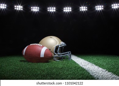 Football and gold helmet on grass field below stadium lights at night - Powered by Shutterstock