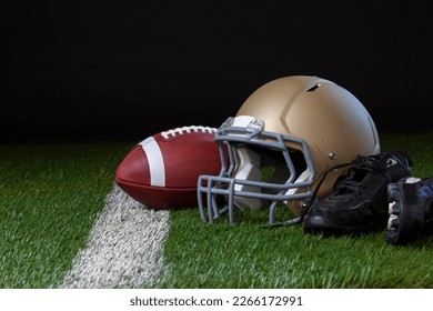 Football helmet with football and cleats on a grass field with a white stripe and dark background - Powered by Shutterstock
