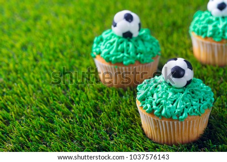 Football party, birthday decorated cupcake on green grass background. Copy space.