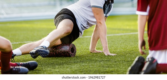 Football physiotherapist personal trainer using foam roller. Trainer showing exercises to kids soccer players in a team. Football stretching session in school team - Powered by Shutterstock