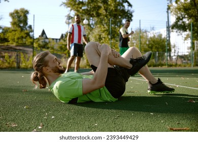 Football player holding injured knee leg lying on field, accident during game - Powered by Shutterstock