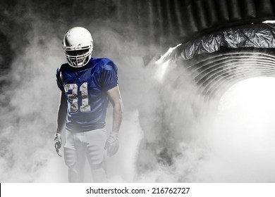 Football player, on a blue uniform, leaving a smoky tunnel, ready to get on the field.