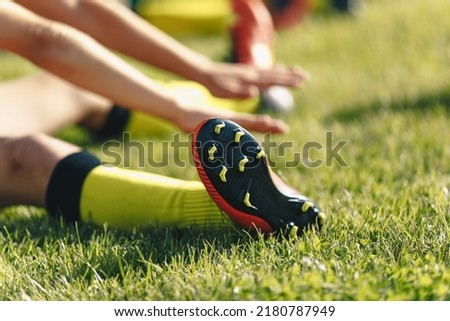 Football Player Stretches Sitting on Grass Pitch. Stretching Session After Workout For Footballers. Player in Soccer Cleats and Socks