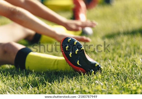 Football Player Stretches Sitting on Grass Pitch.\
Stretching Session After Workout For Footballers. Player in Soccer\
Cleats and Socks