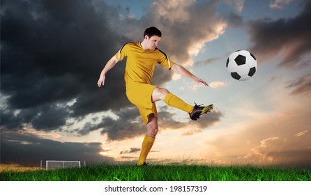 Football player in yellow kicking against green grass under blue and orange sky - Powered by Shutterstock