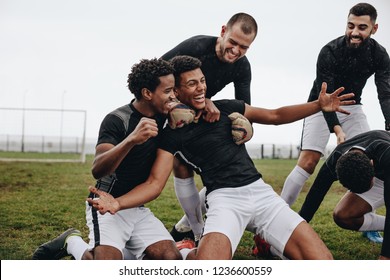 Football players celebrating success on the field. Happy footballer sitting on his knees with open arms after scoring a goal being cheered by his teammates. - Powered by Shutterstock