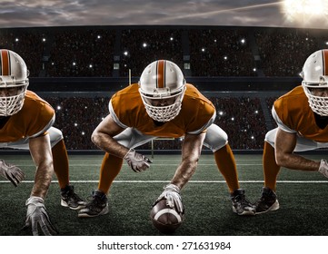 Football Players with a orange uniform on the scrimmage line, on a stadium.