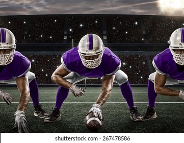 Football Players with a purple uniform on the scrimmage line, on a stadium.