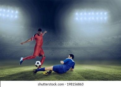 Football players tackling for the ball against large football stadium under blue sky - Powered by Shutterstock