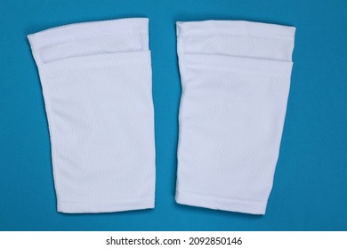 Football shin guards in white fabric. Shin sleeves made of polyester on a light blue background. White shield holders. Football ammunition for athletes. 