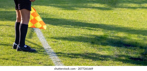 Football soccer arbiter assistant with flag at hands. Blurred green field background, close up.
