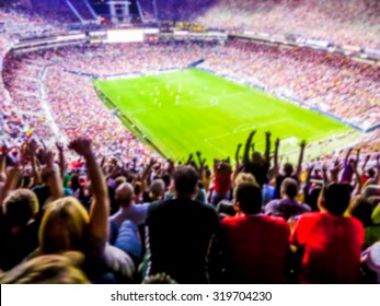 Футбольные болельщики поддерживают свою команду и празднуют гол на полном стадионе под открытым небом с красивым небом. - Размытие картины.