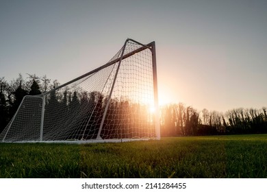 Football Or Soccer Goal Post On A Green Grass Pitch In A Park At Sunset Time. Nobody. Calm Mood. Sun Flare. Sport Theme Background