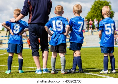 Football Soccer Match Game For Children. Youth Sports Team With Soccer Coach During Football Match At The Stadium. Kids Reserve Players Waiting On A Bench With Coach And Watching Soccer Match.