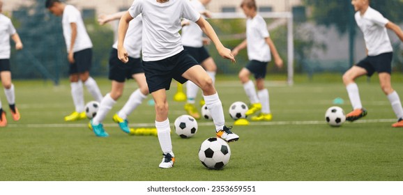 Football soccer school for youth boys. Group of teenage boys kicking soccer balls during a training session. Kids play soccer training games on the training pitch. School kids in white jersey shirts - Powered by Shutterstock