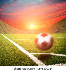 Football Stadium With A Black And White Ball In Motion On A Corner Of A Field With Green Grass Against A Sky With A Sunset