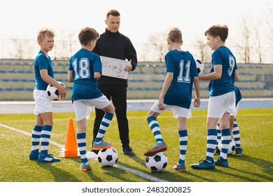 Football tactics training for children. Boys with a coach on the football field. Coach talking about the game plan. Trainer using tactics board to explain soccer game strategy - Powered by Shutterstock