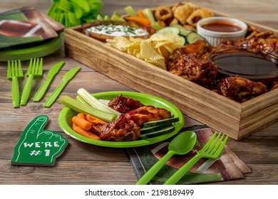 Football Tailgate Themed Party Food Display With Chicken Wings, Sauces, Dips, Wieners, Veggies, Chips, Pretzels In Wooden Tray With Football Plates, Napkins And Decorations Shot Sitting On Wood Table