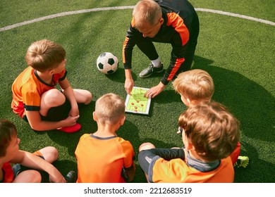 Football training. Soccer coach explaining game rules and strategy using tablet, map. Sports junior team sitting on grass pitch with trainer. Concept of sport, achievements, studying, goals, skills - Powered by Shutterstock