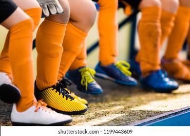 Footballers in soccer cleats. Youth athletes in soccer clothes. Young football players wearing football clothes and soccer shoes sitting on bench in a row. Soccer detail background. - Powered by Shutterstock