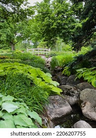 Footbridge Over Brook. Flowery Brook Garden, Flowerbeds Laid Out In Typical English Style, Unconstrained By Symmetry Or Straight Lines. Montreal Botanical Garden. An Impressionist Landscape.