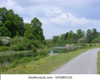 foothpath besides river lined with trees in summer with sky