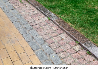 A Footpath Made Of Tiles Of Different Types Of Stone And A Granite Curb In The Park With A Green Trova In The Park.