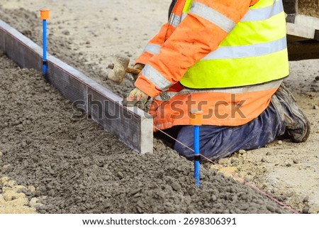 Footpath under construction. Builder installing new edging pin kerbs on concrete