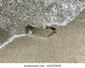 Footprint On Sand Washing Out By Sea Wave Close-up. People Disappear Concept