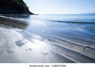 Footprints of human feet on the black sand beach on sunny summer, art shape of wavy sandy, sunny glittering on ripples waves, a tranquil seascape of Koh Chang Island, Ranong, Thailand.