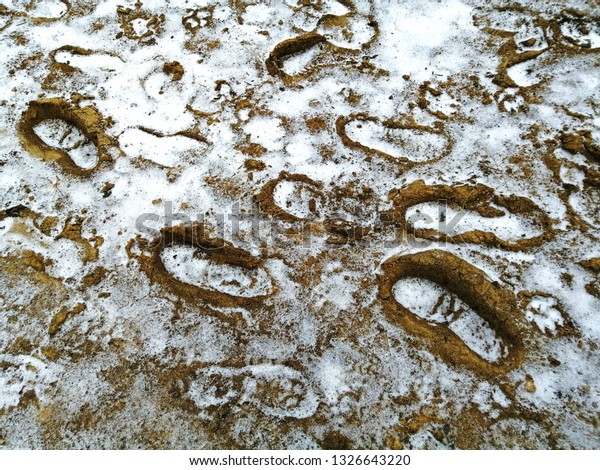 Footprints on the clay ground covered with\
snow. Texture. Abstract\
background.