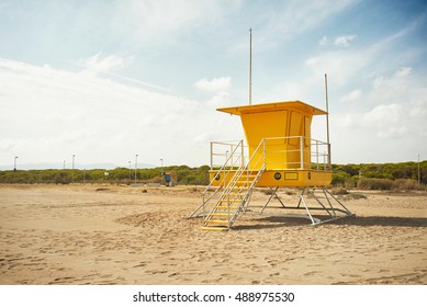 Footprints on an empty beach around a bright yellow lifeguard post Commercial image