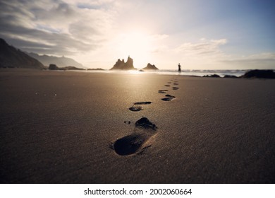 Footprints in sand against silhouette of person. Man walking along beach to sea at golden sunset. Tenerife, Canary Islands, Spain. - Shutterstock ID 2002060664
