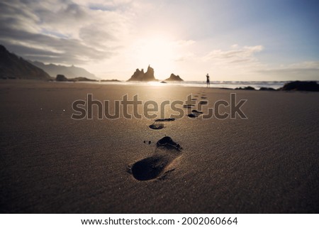 Footprints in sand against silhouette of person. Man walking along beach to sea at golden sunset. Tenerife, Canary Islands, Spain.