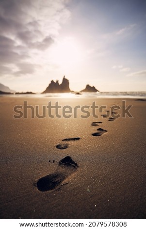 Footprints in sand on beach leading to sea. Golden sunset in Tenerife, Canary Islands, Spain.
