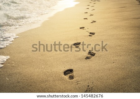 Footprints in the sand at sunset. Beautiful sandy tropical beach with sea waves. Footsteps on the shore.