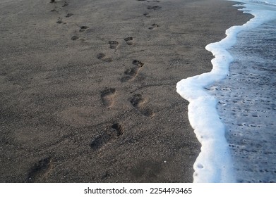 Footprints and white foam waves on the black sand on the beach. Footprints pattern on sands background. Sea wave sand backgrounds.