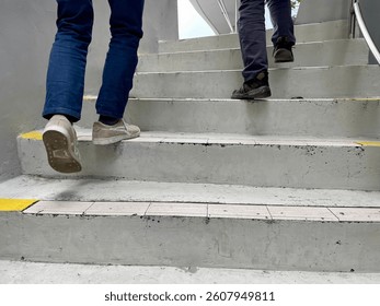 The footsteps of two men wearing shoes and trousers climbing the gray cement stairs. - Powered by Shutterstock - Get 15% off with code: PIKWIZARD15