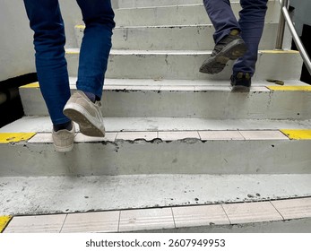 The footsteps of two men wearing shoes and trousers climbing the gray cement stairs. - Powered by Shutterstock - Get 15% off with code: PIKWIZARD15
