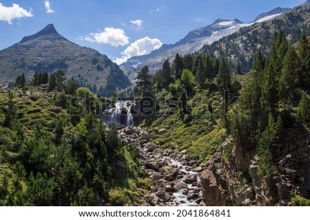 Forau d'Aigualluts waterfall with mountains and Aneto snowy peak in the background, in Benasque, Huesca, Spain. Alpine landscape in Posets Maladeta natural park, Spanish Pyrenees