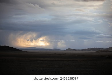 Forboding clouds loom over a dark, open landscape and the headlights of a car moving away from the storm.