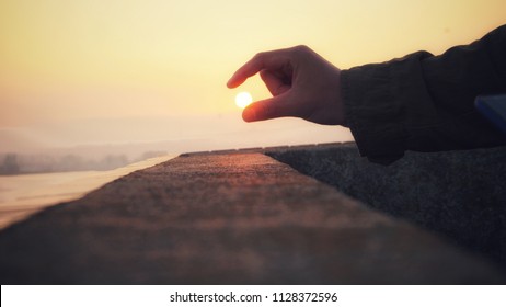 A Forced Perspective Image Of A Man Picking The Sun From The Golden Sky.