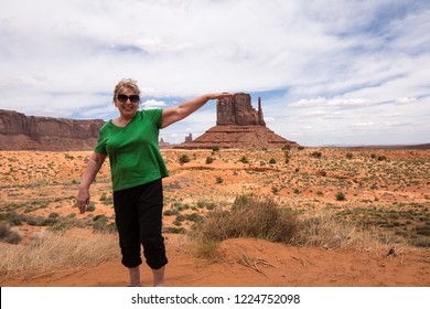 Forced Perspective Of A Senior Adult Woman (60s) Pretending To Touch A Famous Rock Formation In Utah Monument Valley