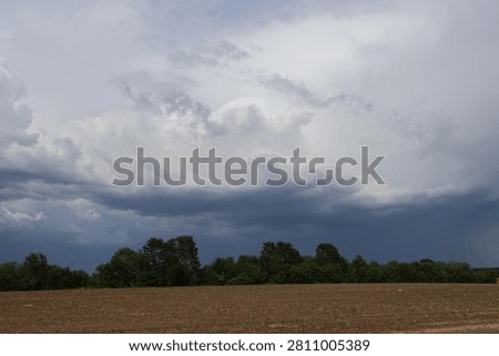 Foreboding storm clouds forming above a flat cultivated field with a line of trees