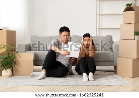 Foreclosure And Repossession Concept. Scared asian couple looking at eviction notice, sitting on the floor, empty space