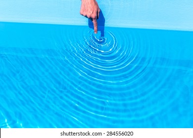 Forefinger Making Circular Waves In Water Of Blue Swimming Pool