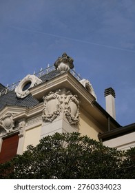 Foreground features a neoclassical building, while a jet plane streaks across the bright blue sky, leaving a long contrail behind.