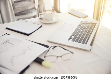 Foreground of objects on the working place: eyeglasses, diagrammes, laptop, notebook